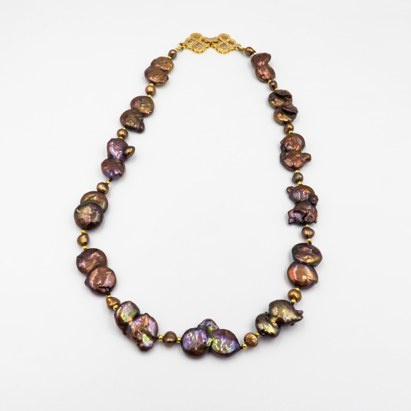 שרשרת נדירה שמדברת בעד עצמה המורכבת מפניני בארוק טבעיות בגוון שוקולד עמוק, עם אביזרים בציפוי זהב שמדגישים את צורתן הבלתי אחידה והמרקם החי של כל פנינה. הברק המטאלי החם של הפנינים משתלב באופן הרמוני עם הנגיעות המוזהבות, ויוצר תחושה של חומר חי ונושם. השראה מהטבע עם קריצה עיצובית מודרנית – אידיאלי לאירוע ערב, להופעה עם אמירה או כמתנה מרשימה לאישה מיוחדת. פניני הבארוק, כל אחת עם אישיות משלה, הופכות את השרשרת הזו לתכשיט שמבליט את הייחוד שלך בלי מילים.