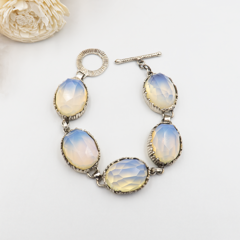 צמיד כסף סטרלינג בעבודת יד, בעל חמש אבני אופליט בגוון אופל שמיימי – תערובת עדינה של תכלת, לבן ושמנת. סוגר טי דקורטיבי מעניק גימור אלגנטי וקל לשימוש. צמיד ייחודי ונשי שמתאים לאירועים חגיגיים כמו חתונה, בר מצווה או חג, וגם לשימוש יומיומי עם טוויסט אלגנטי. תכשיט עם מראה אל-זמני ורוך מרגש.

