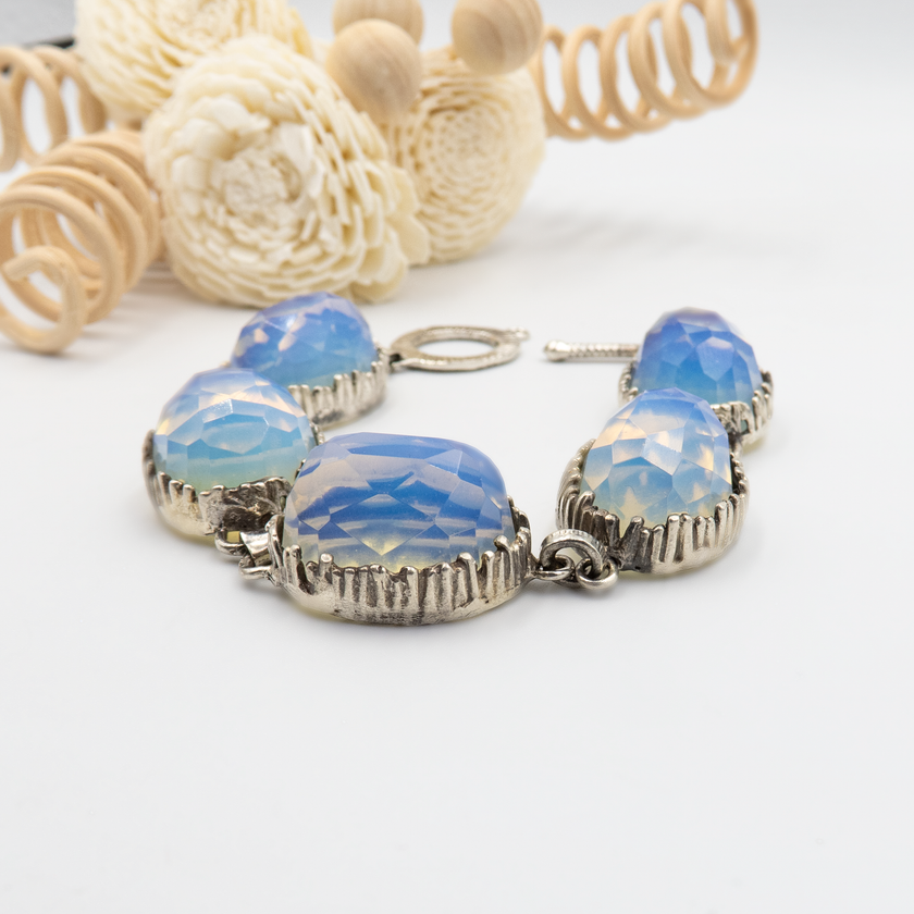 צמיד אובאלי מכסף סטרלינג, משובץ באופליטים בגימור פאות נוצץ – כל אבן בעלת גוון שמנת-כחול רך, המשווה לתכשיט מראה מהפנט ועדין כאחד. מתאים לנשים שאוהבות עיצוב ייחודי אך לא מצועצע. הצמיד ננעל באמצעות סוגר טי עגול, מוסיף מגע וינטג’י מודרני. בחירה נהדרת כמתנה עם משמעות – רומנטית, רגישה ומרשימה.

