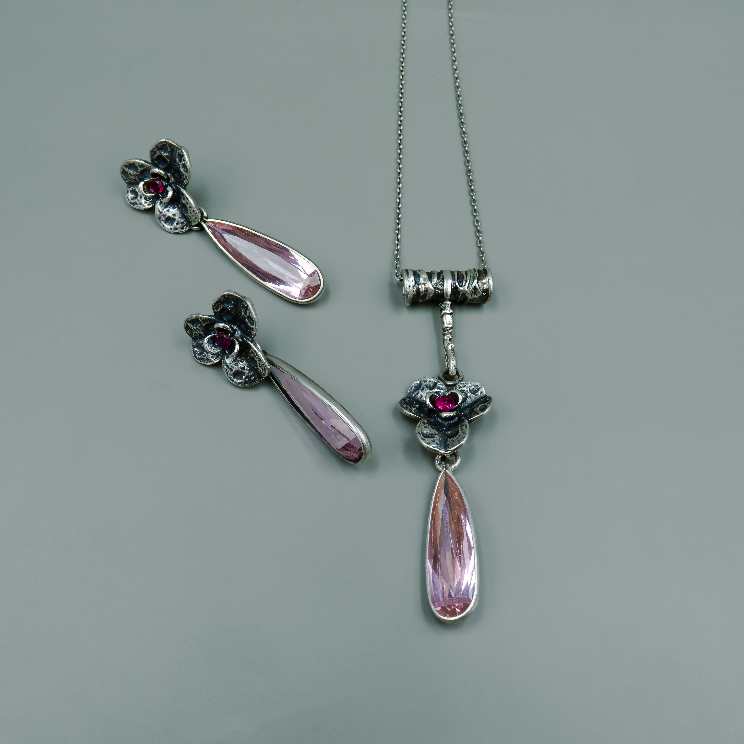 שרשרת כסף עם תליון בצורת פרח עתיק, בעל עלים מפורטים ואבן קטנה בגוון פוקסיה במרכזו. אבן הטיפה הארוכה בגוון ורוד שקוף משתלשלת מהפרח ומוסיפה מגע רך ונשי. שילוב בין עיצוב וינטג' קלאסי למראה מודרני ונועז. מתאים לכל מי שמחפשת תכשיט עם אמירה, שהוא גם ייחודי, גם רך וגם מלא אופי. משתלב נהדר עם שמלות רומנטיות או כאביזר מיוחד למראה ערב.

העגילים להמחשה בלבד