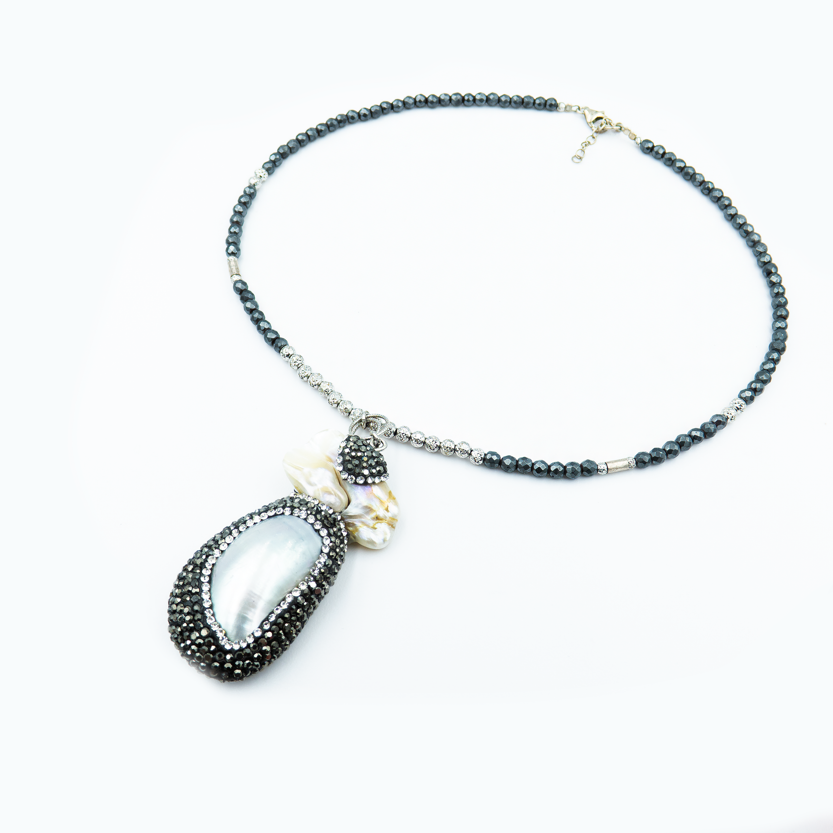 כמו אוצר מהים – תליון ייחודי עשוי צדף לבן שנראה כאילו נשטף הרגע אל החוף, עטוף באלפי קריסטלים שחורים נוצצים. השרשרת משלבת חרוזים כהים בגווני המעמקים, ומשדרת תחושת עומק, מסתורין ויוקרה טבעית.