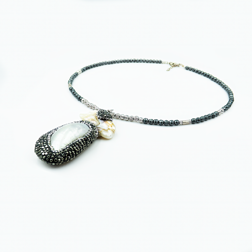 תכשיט שמשלב עוצמה ועדינות – תליון פנינה גדול עם נצנוץ ייחודי מוקף קריסטלים כהים, תלוי משרשרת חרוזים שחורים מבריקים. מתאים לערב או אירוע מיוחד, עם שמלה שחורה או חולצה לבנה קלאסית. נוכחות שאי אפשר להתעלם ממנה.