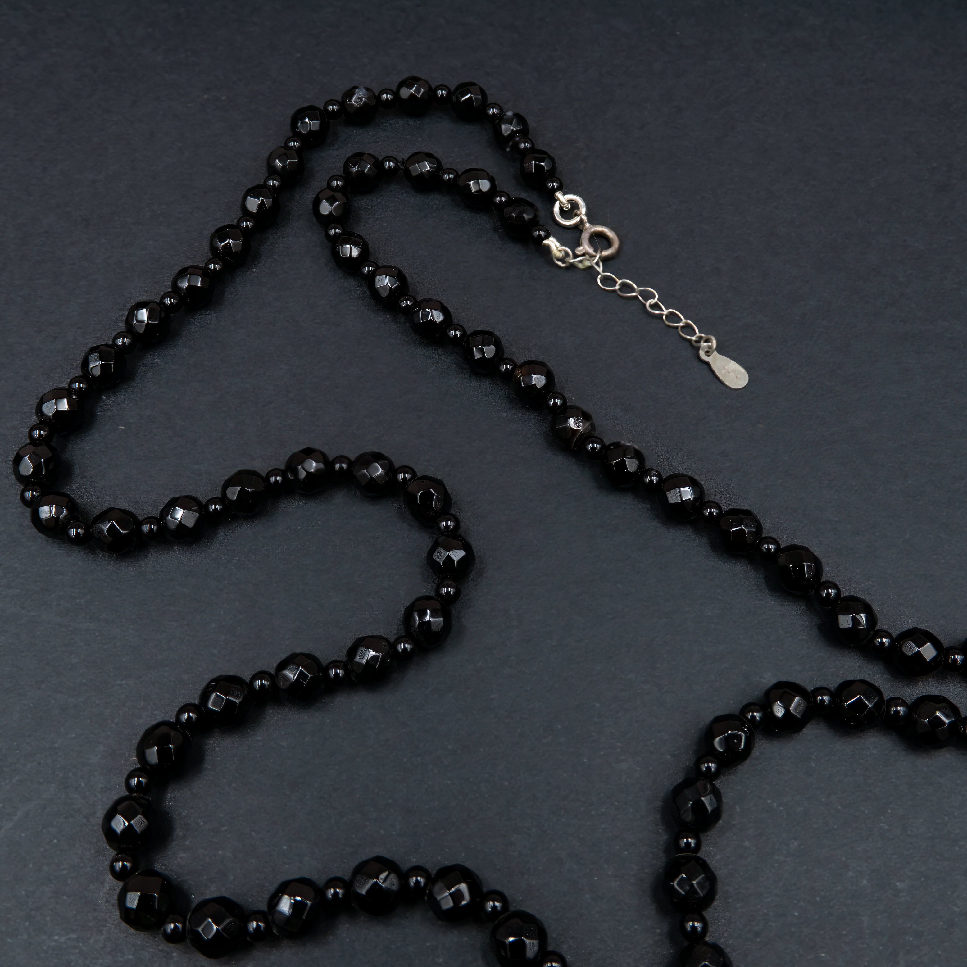 תכשיט דרמטי בגוונים שחורים עם נגיעות זוהר, משולבות בחרוזים קטנים וגדיל דרמטי – תכשיט עם נוכחות אלגנטית ותחושת עוצמה. האבנים השחורות יוצרות מראה עמוק ומתוחכם, בעוד שהגדיל מעניק זרימה רכה ונוכחות עוצמתית. הענק משתלב באופן מושלם עם לבוש ערב או מראה קז'ואל מהודר, ומשדר איזון בין יוקרה שקטה ותחכום עיצובי. כל אבן אוניקס נבחרת בקפידה, מה שמבטיח תכשיט איכותי, מדויק ובעל אמירה עיצובית חזקה. מתאים לנשים שאוהבות לבלוט בעדינות – תכשיט שהוא גם תוספת, וגם מרכז ההופעה.