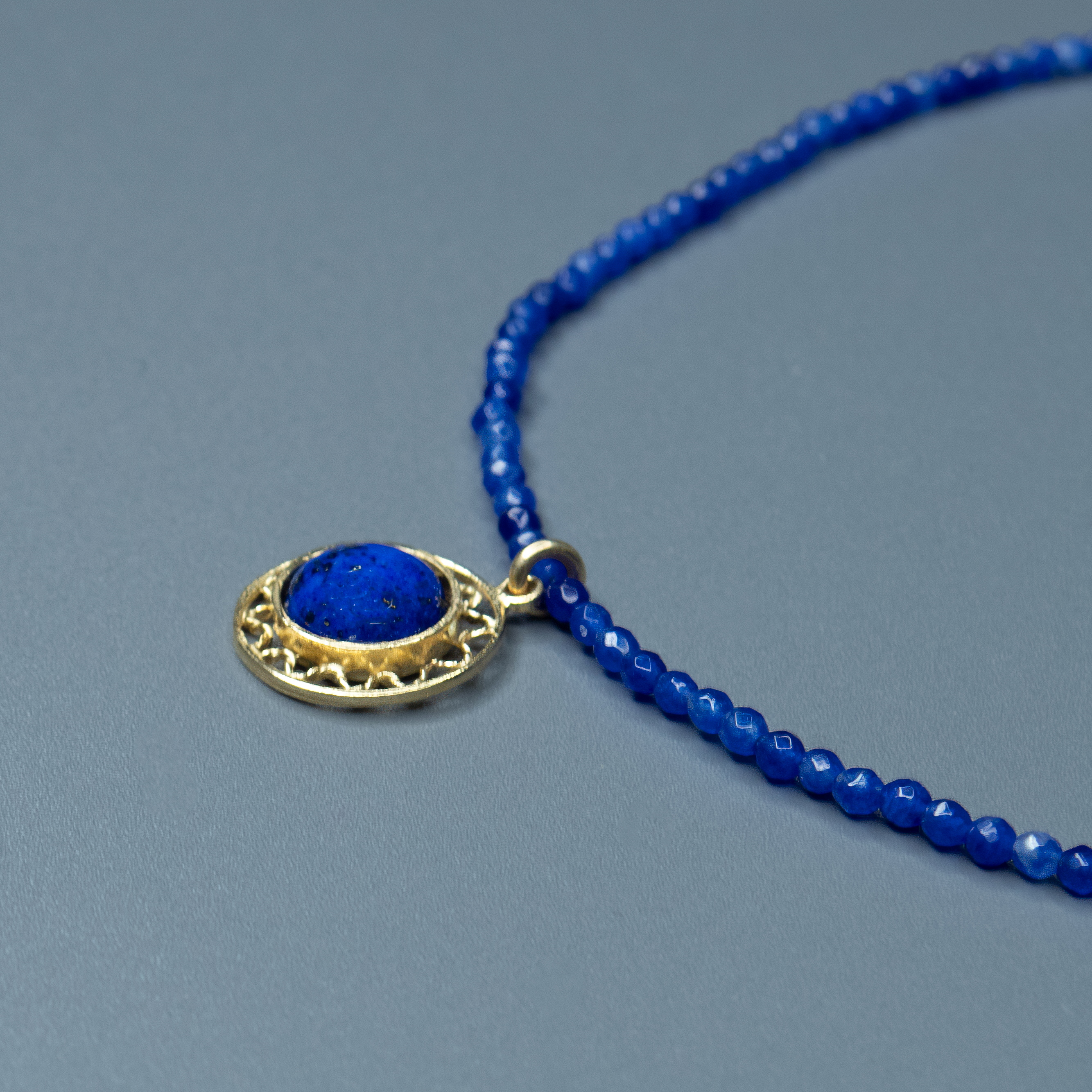 שרשרת קולר עדינה עשויה חרוזים כחולים כהים, כמו שמיים ליליים זרועים כוכבים, ובמרכזה תליון עגול מוזהב עם אבן כחולה בוהקת בלבו – דומה למראה הירח המלא מעל ים עמוק. העיצוב הקלאסי משתלב בהרמוניה עם האלמנטים הגאומטריים, ויוצר מראה של איזון והרמוניה. תכשיט מושלם למי שמבקשת להוסיף מגע של עומק שקט ואור פנימי לכל הופעה.