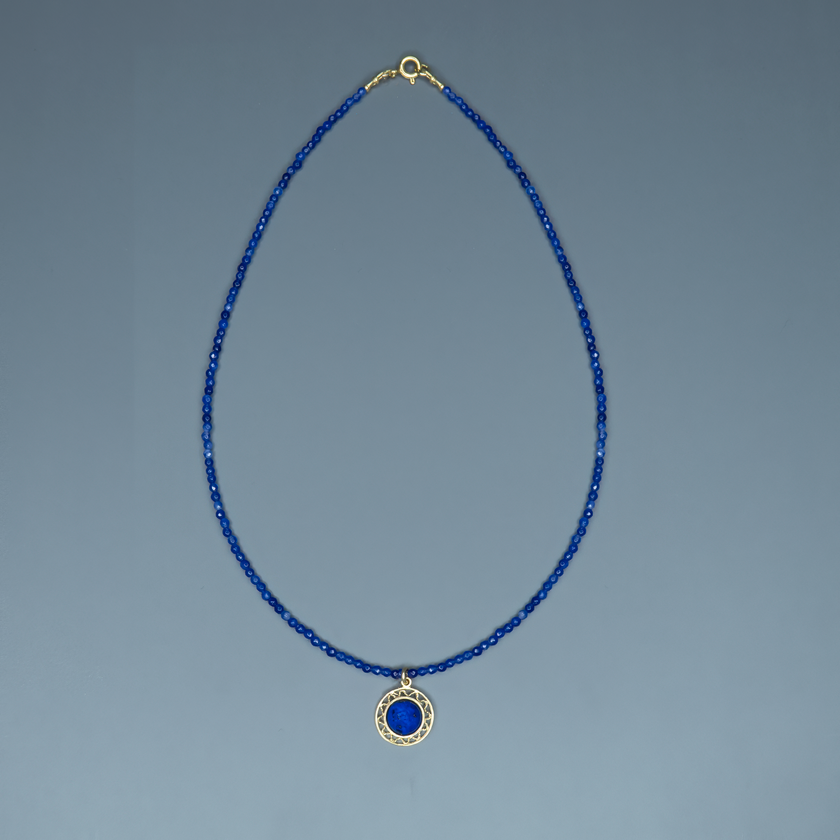 שרשרת קולר בגוון כחול עמוק עם תליון מוזהב עגול, שבתוכו משובצת אבן כחולה מבריקה, יוצרת מראה יוקרתי אך מודרני. החרוזים הקטנים מעניקים תחושת דיוק ועדינות, בעוד שהתליון מוסיף נוכחות מרשימה. מונחת על צוואר נקי שמדגיש את עיצוב השרשרת, והצילום מדגיש את קווי המתאר הנשיים. תכשיט מושלם לערב אלגנטי, אירוע עסקי או מתנה מתחשבת עם הרבה סטייל.