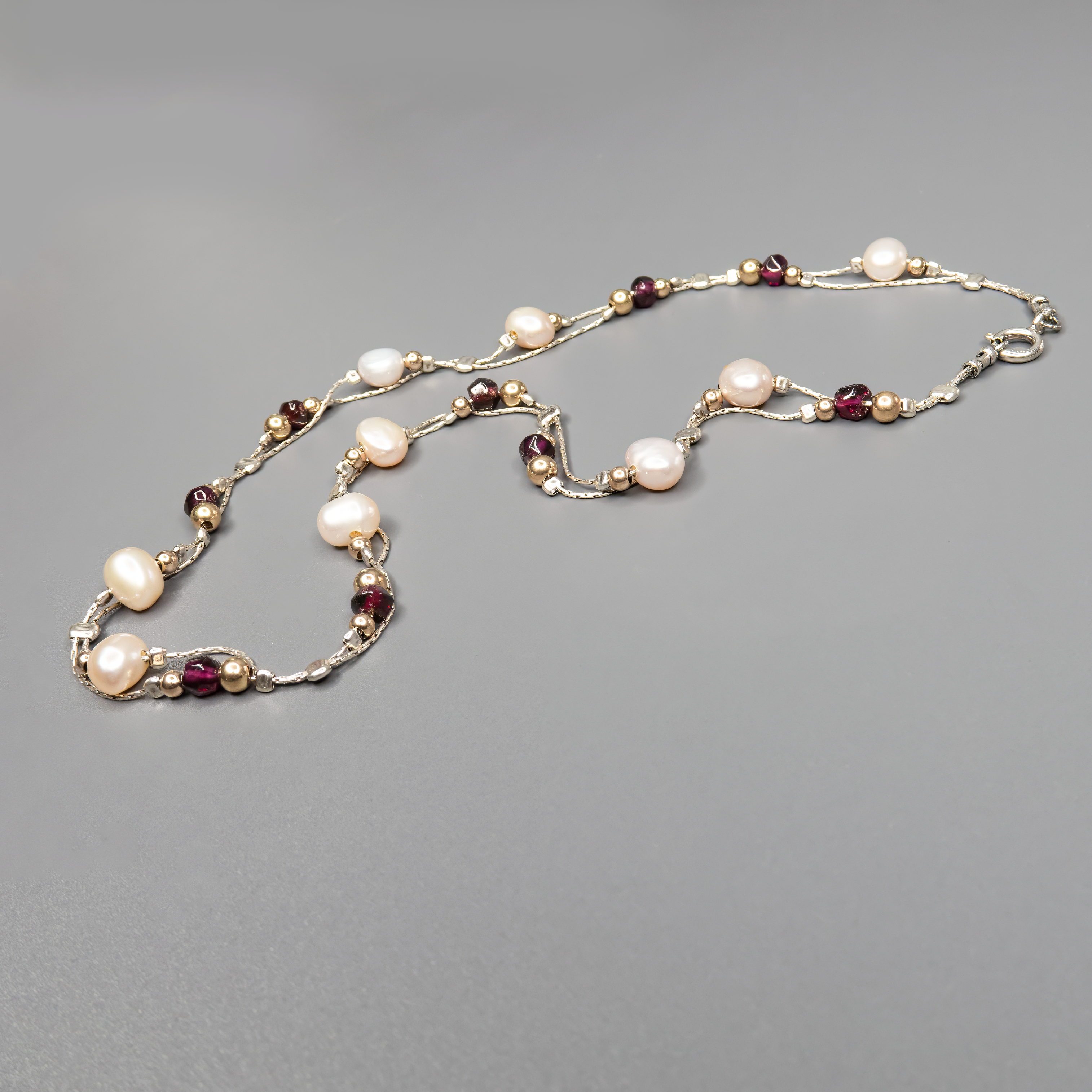 שרשרת כסף בעבודת יד המשלבת פנינים לבנות טבעיות עם גרנטים עמוקים בגוון יין – עיצוב עם ניגוד הרמוני בין אלגנטיות ועדינות לבין צבע וחום. הפנינים מוסיפות אור ורכות לכל הופעה, בעוד שהגרנטים מביאים עומק, חמימות ונשיות עם נוכחות שקטה ומרגשת. השרשרת עשויה מכסף סטרלינג 925, עם סגירה מעודנת שמשלימה את הקו האלגנטי של התכשיט. תכשיט שמתאים לאירועים מיוחדים אך גם לבעלות סגנון אישי שמבקשות לשלב מראה על־זמני עם קריצה עדכנית.