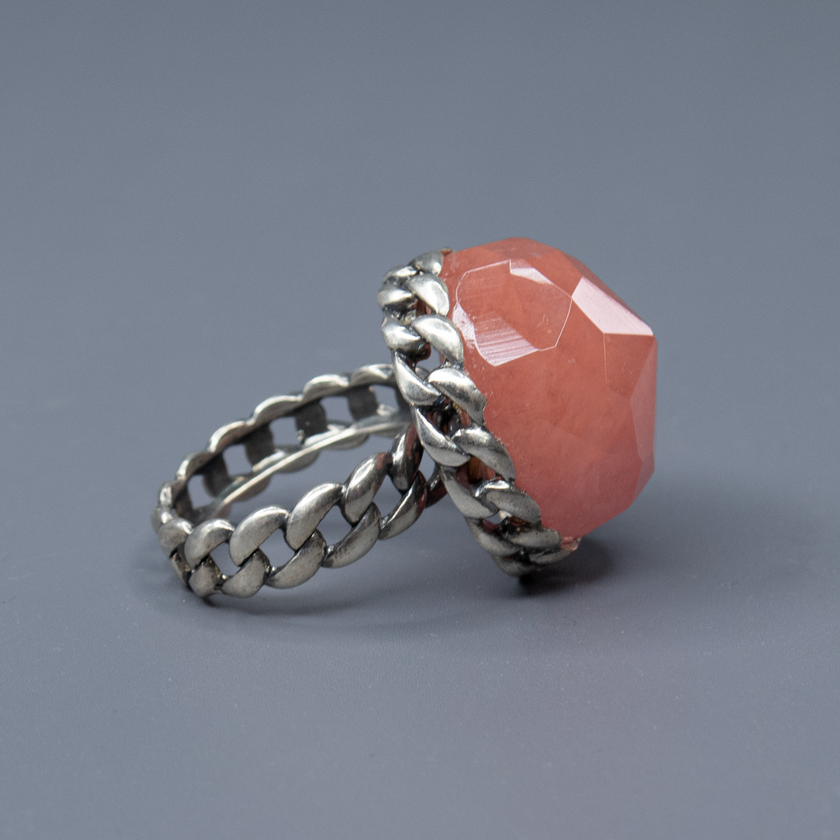 טבעת כסף דרמטית בהכנה קפדנית, מעוטרת באבן גדולה בגוון ורוד־קורל עם חיתוך פאות (faceted) שמדגיש את הברק והעומק של האבן. העיצוב משלב בסיס כסף בעבודת חריטה בדוגמה קלועה, המעניק לטבעת מראה חזק אך אלגנטי, שמזכיר טבעת שרשרת או סגנון בוהו וינטג' מתוחכם. האבן הגדולה הופכת את הטבעת לטבעת יוצאת דופן, כזה שלא עובר מתחת לרדאר, אך שומר על איזון אסתטי. גוון האבן מחמיא לעור, מתאים לקיץ ולחורף כאחד, ויוצר ניגוד יפהפה עם גוון המתכת. תכשיט מיוחד שמדגיש אישיות, טעם ייחודי ואמירה אישית לא שגרתית. מושלמת כטבעת מתנה, ליום־יום או