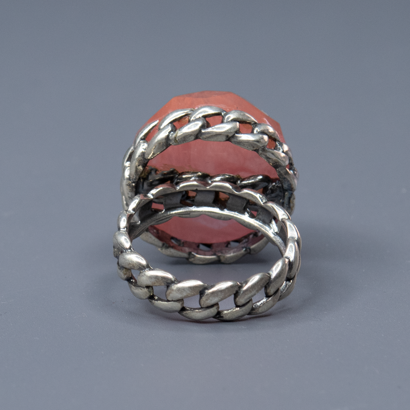 טבעת כסף ייחודית בהכנה קפדנית, מקושטת באבן גדולה בגוון ורוד־קורל עם חיתוך פאות (faceted) שמבליט את הזוהר את הברק והעומק של האבן. העיצוב משלב בסיס כסף בעבודת חריטה בעיצוב ארוג, המעניק לטבעת מראה חזק אך אלגנטי, שמזכיר טבעת שרשרת או סגנון בוהו וינטג' מתוחכם. האבן הגדולה הופכת את הטבעת לאקססורי בולט, כזה שלא עובר מתחת לרדאר, אך שומר על איזון אסתטי. גוון האבן מחמיא לעור, מתאים לקיץ ולחורף כאחד, ויוצר ניגוד יפהפה עם גוון המתכת. תכשיט מיוחד שמדגיש אישיות, עין לעיצוב ואמירה אישית לא שגרתית. מושלמת כטבעת מתנה, ליום־