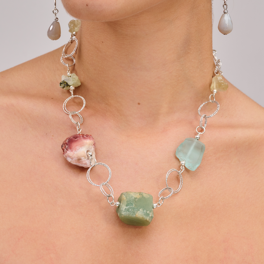 שרשרת כסף בעבודת יד שמשלבת מגוון עשיר של קריסטלים טבעיים – אמטיסט בגוון סגול עמוק, רוז קוורץ ורדרד ורך, פלואוריט בגוני ירוק וסגול שקופים, וקרנליאן חם בצבע כתום־אדמדם. ההמפגש בין האבנים יוצר איזון אנרגטי עם עומק רגשי ואנרגטי, וכל אבן מוסיפה שכבה משלה של משמעות ונוכחות. השרשרת עוצבה כך שכל אבן תוכל לנשום, ומשלב ביניהן תוך כדי משחק של צבעים, טקסטורות ושקיפויות. השרשרת לנשמות יצירתיות שמתחברות ליופי הרוחני של הטבע, כאלה שמתחברות לעוצמה שקטה ולסטייל ייחודי – וגם לאלו שמחפשות איזון, השראה ורוך. שרשרת שהיא כמו נשי