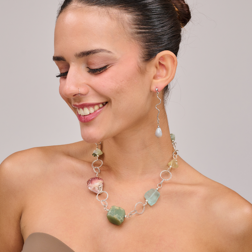 שרשרת כסף בעבודת יד שמשלבת קומבינציה אלגנטית של מינרלים חיים – אמטיסט בגוון סגול עמוק, רוז קוורץ ורדרד ורך, פלואוריט בגוני ירוק וסגול שקופים, וקרנליאן חם בצבע כתום־אדמדם. ההגוונים המתחלפים יוצרים תחושת זרימה עם עומק רגשי ואנרגטי, וכל אבן מוסיפה שכבה משלה של משמעות ונוכחות. התכשיט מדגיש את הברק הטבעי והצבע של כל אבן, ומשלב ביניהן תוך כדי משחק של צבעים, טקסטורות ושקיפויות. השרשרת לנשים שמחפשות עומק ומשמעות באביזרים שלהן, כאלה שמתחברות לעוצמה שקטה ולסטייל ייחודי – וגם לאלו שמחפשות איזון, השראה ורוך. תכשיט שהוא