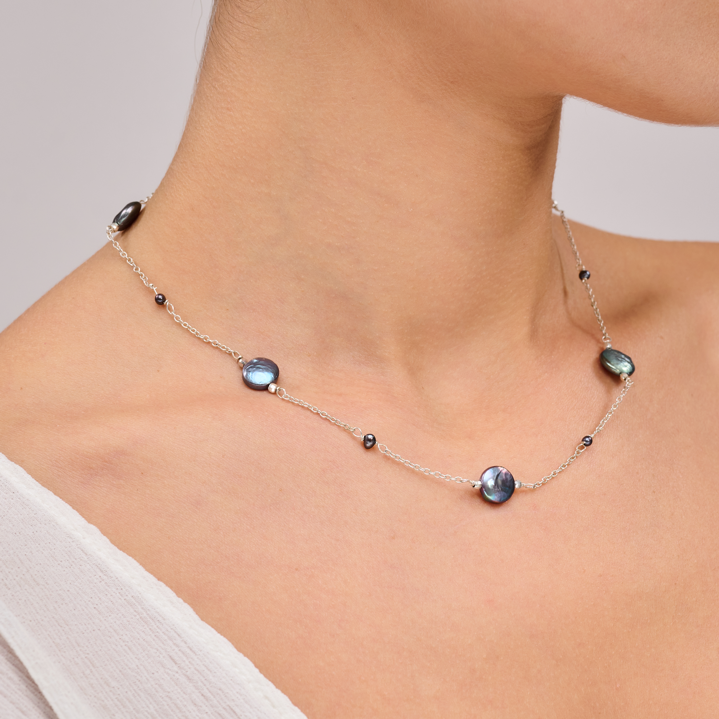 שרשרת מינימליסטית עם פנינים כהות בעבודת יד – תכשיט אלגנטי ונקי, שמשלב מראה מודרני עם עומק צבע טבעי. הפנינים העגולות בגוון אפור־כחלחל כהה משתלבות על גבי שרשרת כסף עדינה ומוסיפות לה נגיעה של יוקרה רגועה. העיצוב עיצוב עכשווי עם גישה על־זמנית – מתאים לנשים שמעדיפות תכשיטים מתוחכמים שאינם צועקים אך אי אפשר להתעלם מהם. השרשרת מושלמת ללבישה יומיומית אלגנטית או כבחירה מושלמת לנשים שמחפשות מראה מאוזן ואלגנטי.