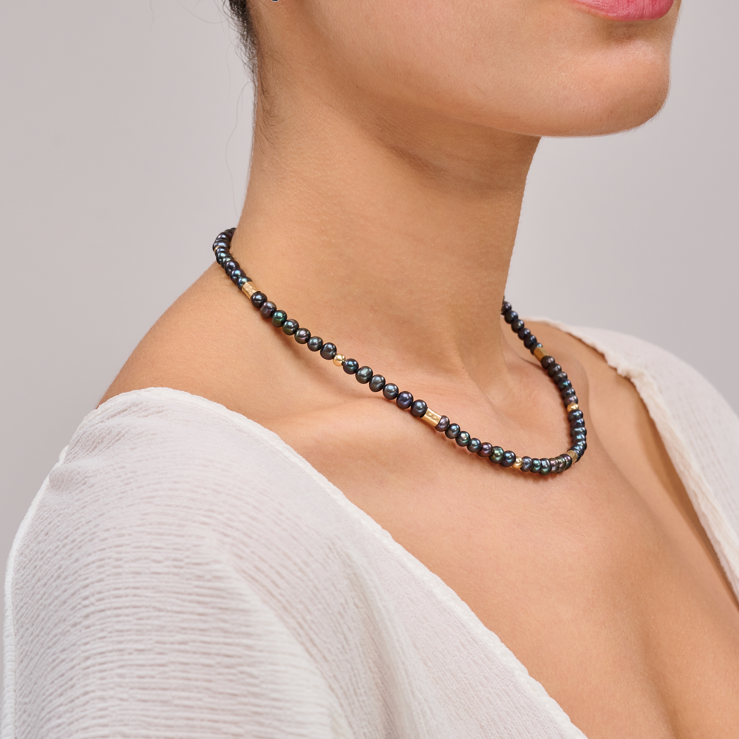 שרשרת צמודה עם פנינים שחורות ואלמנטים מוזהבים – קולר עם אמירה מסוגננת, שמשלב בין עומק אלגנטי לנגיעה חמימה של זהב. הפנינים השחורות יוצרות נוכחות דרמטית אך הרמונית, ואילו חרוזי הגולדפילד מוסיפים קונטרסט זוהר וקו עיצובי נקי אך מרשים. העיצוב הצמוד לצוואר מדגיש את קווי המתאר ומעניק מראה נשי, חזק ומתוחכם. תכשיט מתאים גם לערב וגם ליום, עם מגע של סטייל.