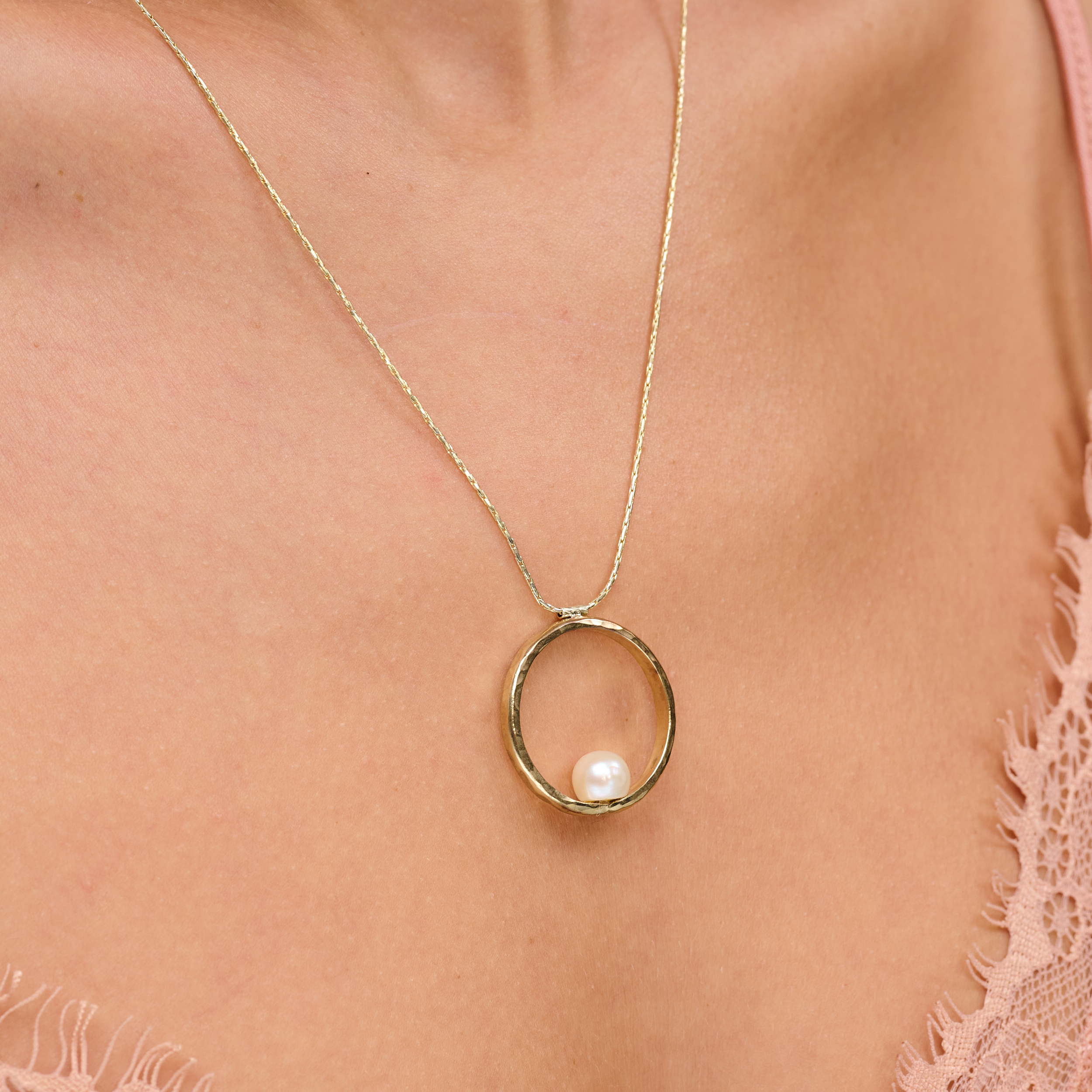 שרשרת בעיצוב אלגנטי עם תליון מוזהב בגודל דומיננטי, המשובץ בפנינה לבנה קלאסית עם ברק טבעי – תכשיט קלאסי בעל נוכחות בולטת. הפנינה ממוקמת במרכז התליון ומקרינה אור רך וטבעי, תוך יצירת ניגוד מחמיא עם הציפוי הזהוב. עיצוב השרשרת משלב בין עידון נשי עם נגיעה עכשווית, ומתאים לאירועים חגיגיים כמו גם ללבוש יומיומי עם נגיעה נשית. פנינים ידועות כמזוהות עם סטייל נשי טהור – ויחד עם הזהב, נוצרת הרמוניה מושלמת בין אלגנטיות לחמימות.