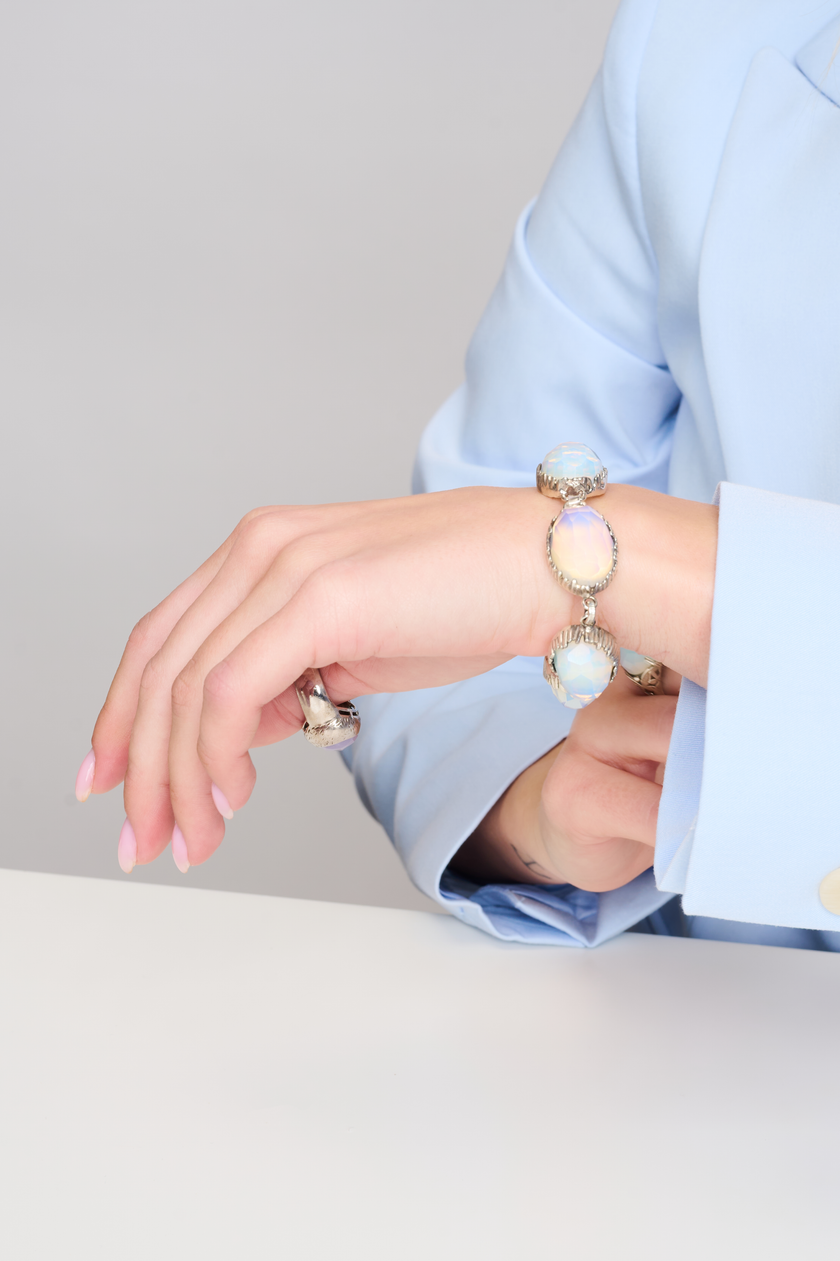 תכשיט בעיצוב יוצא דופן – צמיד מכסף סטרלינג עם חמישה שיבוצים של אופליט בגוון פניני שמשלב כחול, שמנת וזהב עדין באפקט זוהר. האבנים מלוטשות בגימור פאות ליצירת ברק פנימי רך. הצמיד מתאים לנשים שמחפשות מראה ייחודי ועדין, עם נגיעת קסם שמיימית. עיצוב שמחמיא לכל גוון עור ולכל הופעה, יום או ערב.

