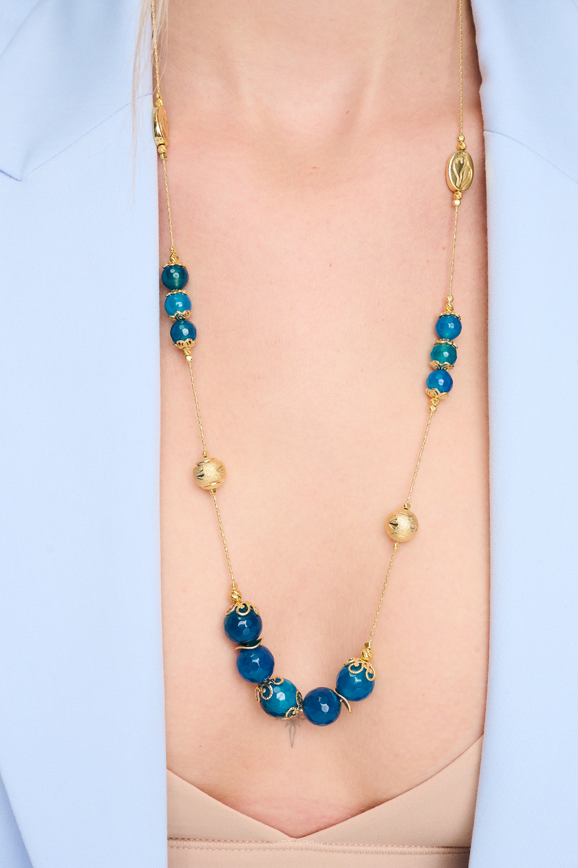 שרשרת ארוכה בעבודת יד מאבני אגט כחולות – עיצוב קלאסי בגווני מים ושקט. החרוזים משתנים בין תכלת בהיר לכחול עמוק, מה שיוצר רכות צבעונית שמרגיעה את המבט. העיצוב הארוך מאפשר גמישות – ניתן לענוד את השרשרת באורך מלא או לעטוף פעמיים למראה רב-שכבתי. אבן האגט נחשבת לאבן הגנה והרגעה, ומוסיפה אנרגיה רגועה שמלווה אותך לאורך היום. תכשיט מושלם למי שמחפשת גם צבע, גם סגנון וגם תחושת חיבור רגשי לטבע.