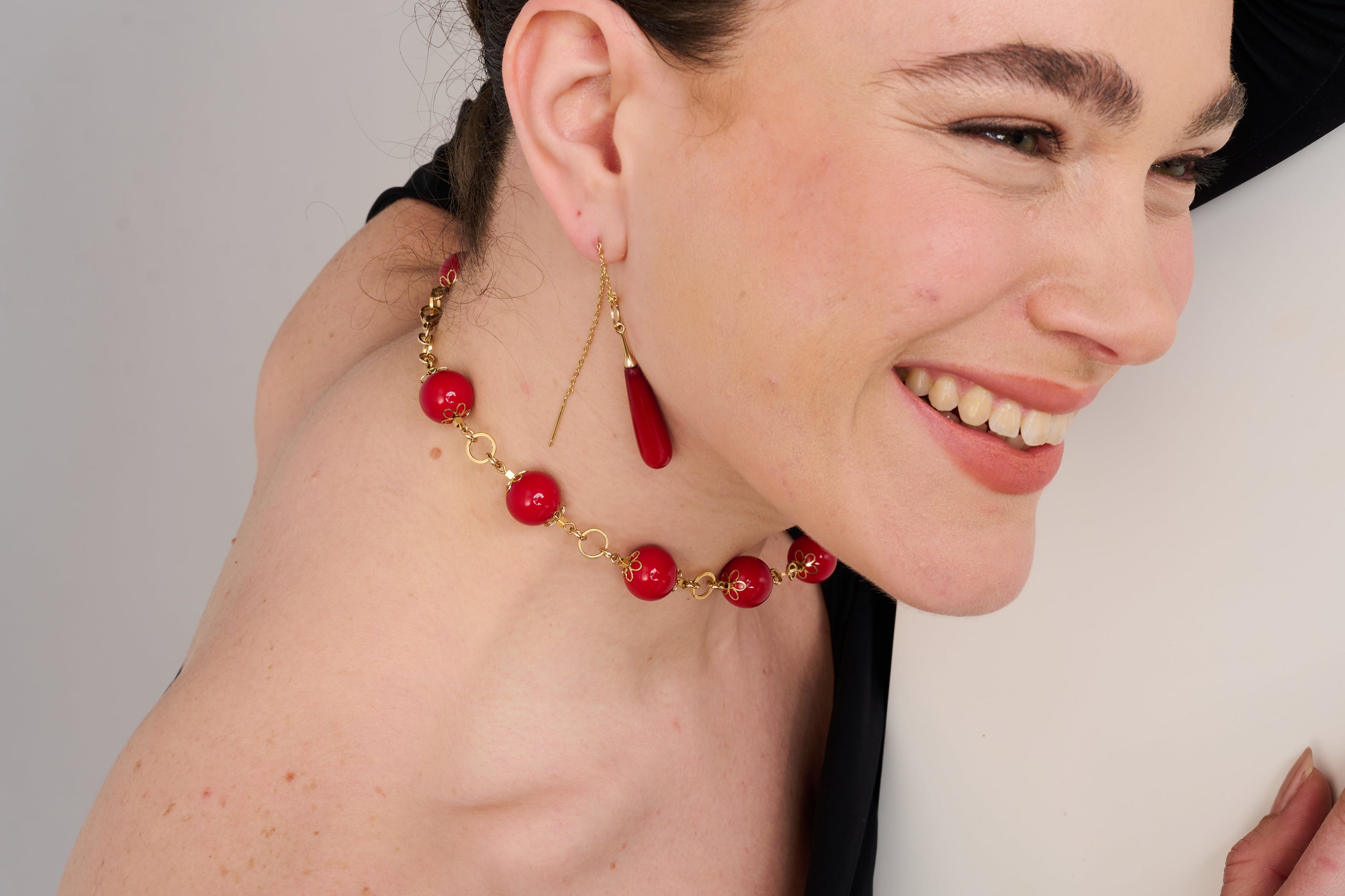 שרשרת עם חרוזים עגולים בגודל מרשים ובצבע אדום עז, משולבים בסוגריים דקורטיביים מוזהבים. החרוזים מחוברים ביניהם בחוליות מוזהבות עבות, ויוצרים תכשיט דומיננטי ואלגנטי שמתאים להצהרה אופנתית. הצילום מתבצע על רקע כהה אשר מדגיש את הברק של החרוזים והמתכת.