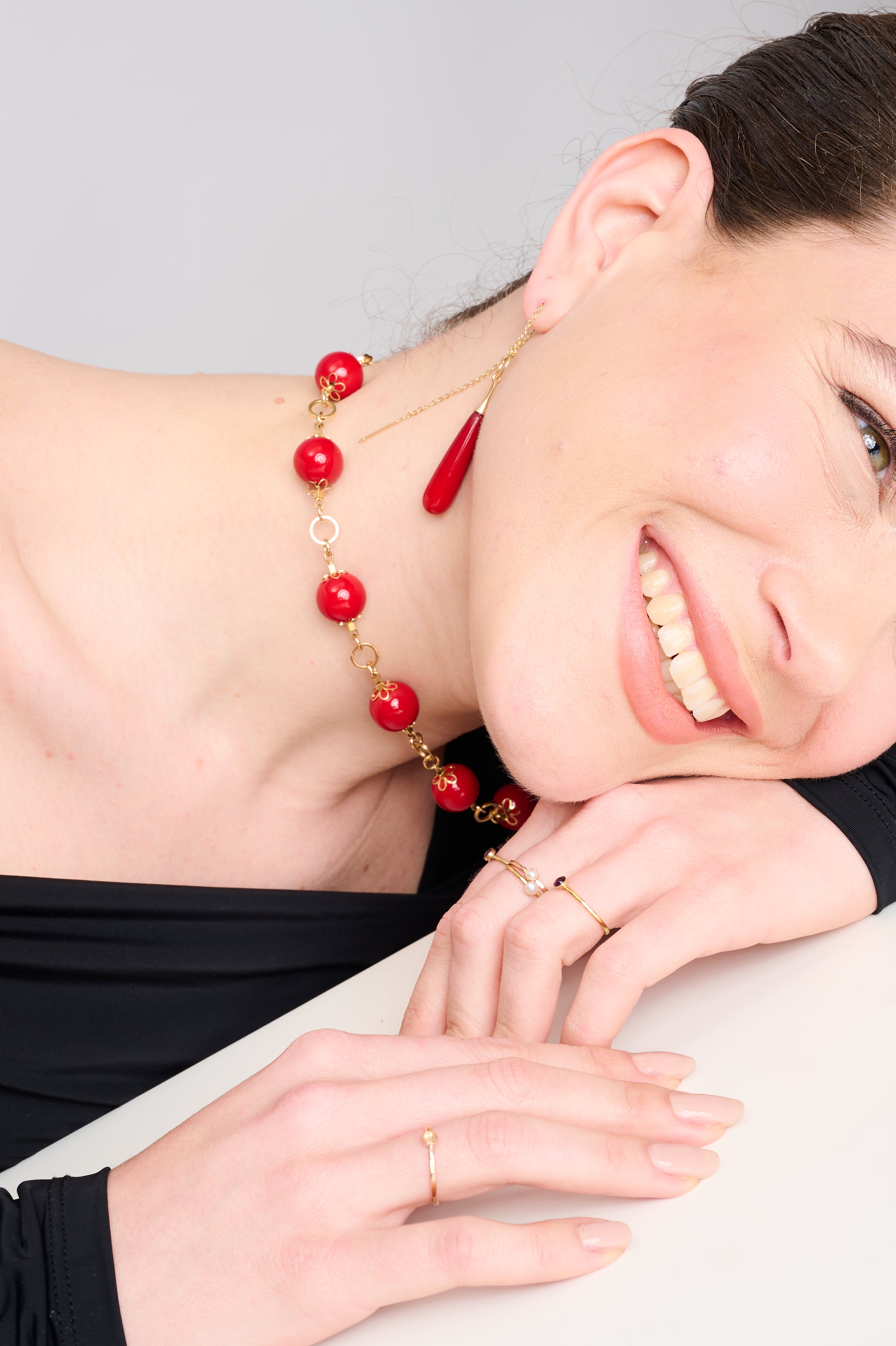 צילום תקריב של שרשרת עם חרוזים עגולים בגוון אדום בוהק, מחוברים בעבודת יד עם מתכת מוזהבת הכוללת עיטורים בצורת פרח. התכשיט שוכן על רקע כהה ומינימליסטי, המדגיש את הברק של הצבעים והעיצוב הקלאסי עם נגיעה מודרנית.