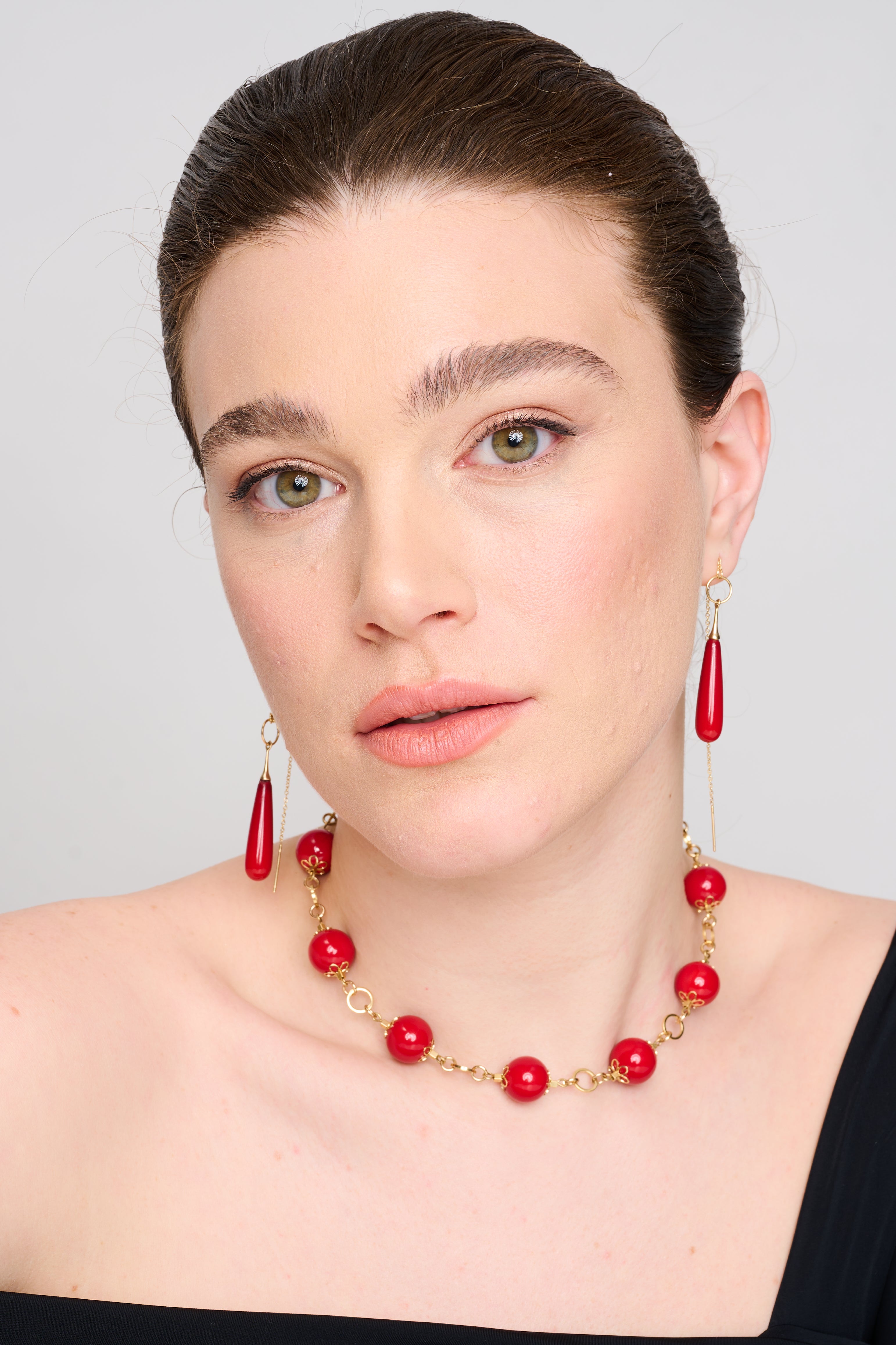 שרשרת חגיגית עם נוכחות חזקה – עשויה חרוזים עגולים בגוון אדום עמוק ומבריק, המחוברים ביניהם באלמנטים מוזהבים בעיצוב פרחוני עדין. התכשיט מוקפד בפרטים, מושך תשומת לב ומתאים לאירועים מיוחדים. הרקע הכהה מוסיף עומק דרמטי לקומפוזיציה.
העגילים להמחשה בלבד