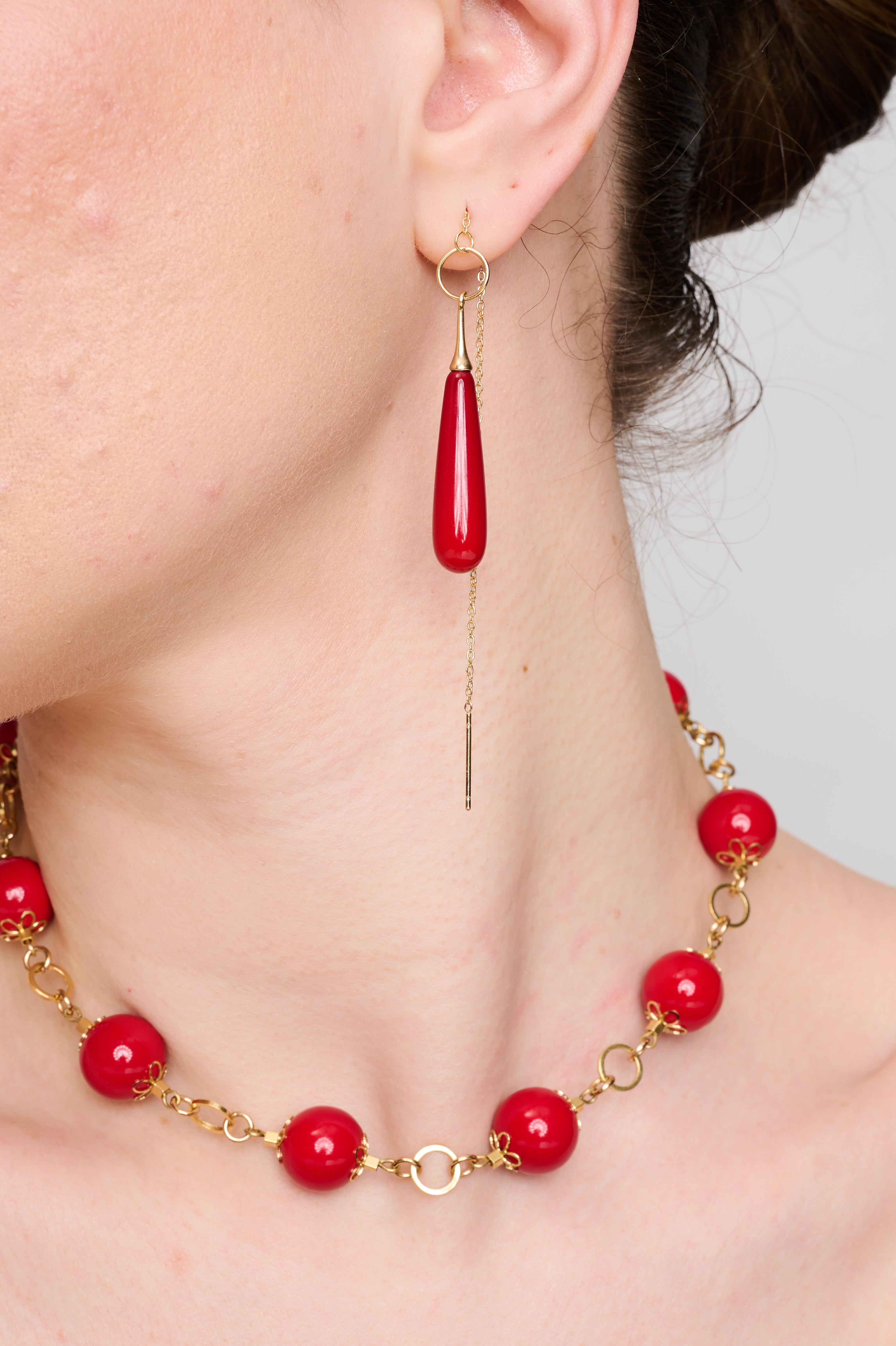 תמונה של שרשרת אופנתית עם חרוזים עגולים בגוון אדום־יין עמוק, בגימור מבריק. כל חרוז מעוטר בעבודת מתכת מוזהבת בצורת עלי כותרת, שמחוברים בטבעות עגולות עבות. הרקע הכהה מקנה לתמונה תחושת יוקרה וניגודיות מרהיבה.
העגילים להמחה בלבד