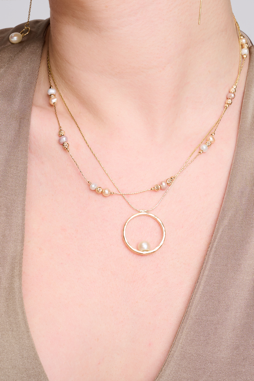 שרשרת בעיצוב אלגנטי עם תליון מרשים בצבע זהב חם, המשובץ בפנינה לבנה קלאסית עם ברק טבעי – תכשיט קלאסי בעל נוכחות בולטת. הפנינה ממוקמת במרכז התליון ומקרינה אור רך וטבעי, תוך יצירת ניגוד מחמיא עם הציפוי הזהוב. עיצוב השרשרת משלב בין עידון נשי עם נגיעה עכשווית, ומתאים לאירועים חגיגיים כמו גם ללבוש יומיומי עם נגיעה נשית. פנינים ידועות כמזכירות יופי טבעי ופשטות אלגנטית – ויחד עם הזהב, נוצרת הרמוניה מושלמת בין אלגנטיות לחמימות.