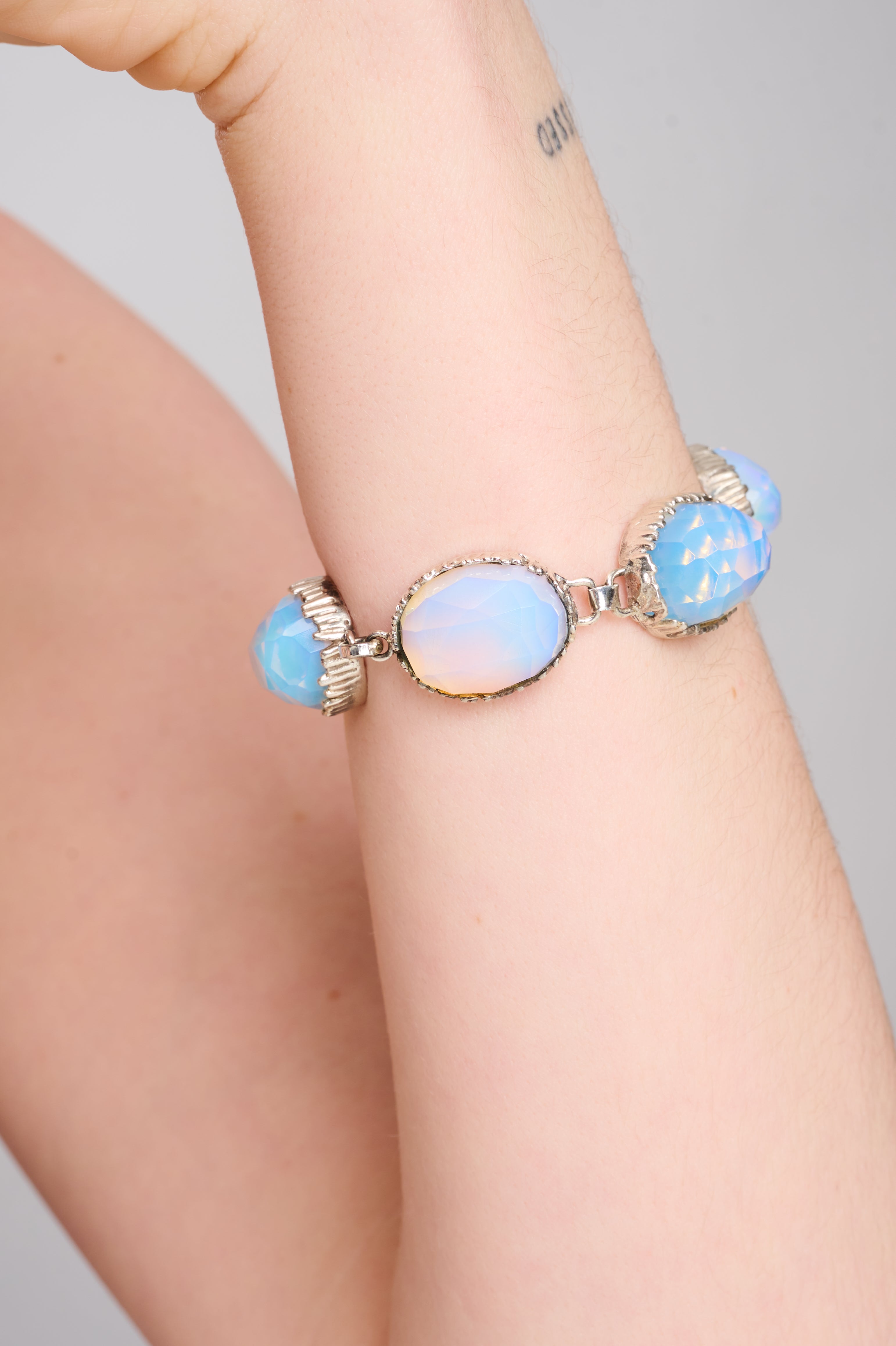 צמיד כסף סטרלינג מעוצב בסגנון קלאסי-רומנטי, עם חמש אבני אופליט אובאליות בגוונים חלומיים של שמנת, כחול וורדרד עדין. כל אבן משובצת במסגרת כסף עשירה בפרטים, עם חיתוך פאות המדגיש את הברק הפנימי והמשחק עם האור. הסוגר המעוצב בטבעת ומוט משלים את המראה באלגנטיות ונוחות. תכשיט שמשרה רוך, נשיות וזוהר שקט – מושלם לערב, לאירוע או כמתנה יוקרתית עם מראה על-זמני.

