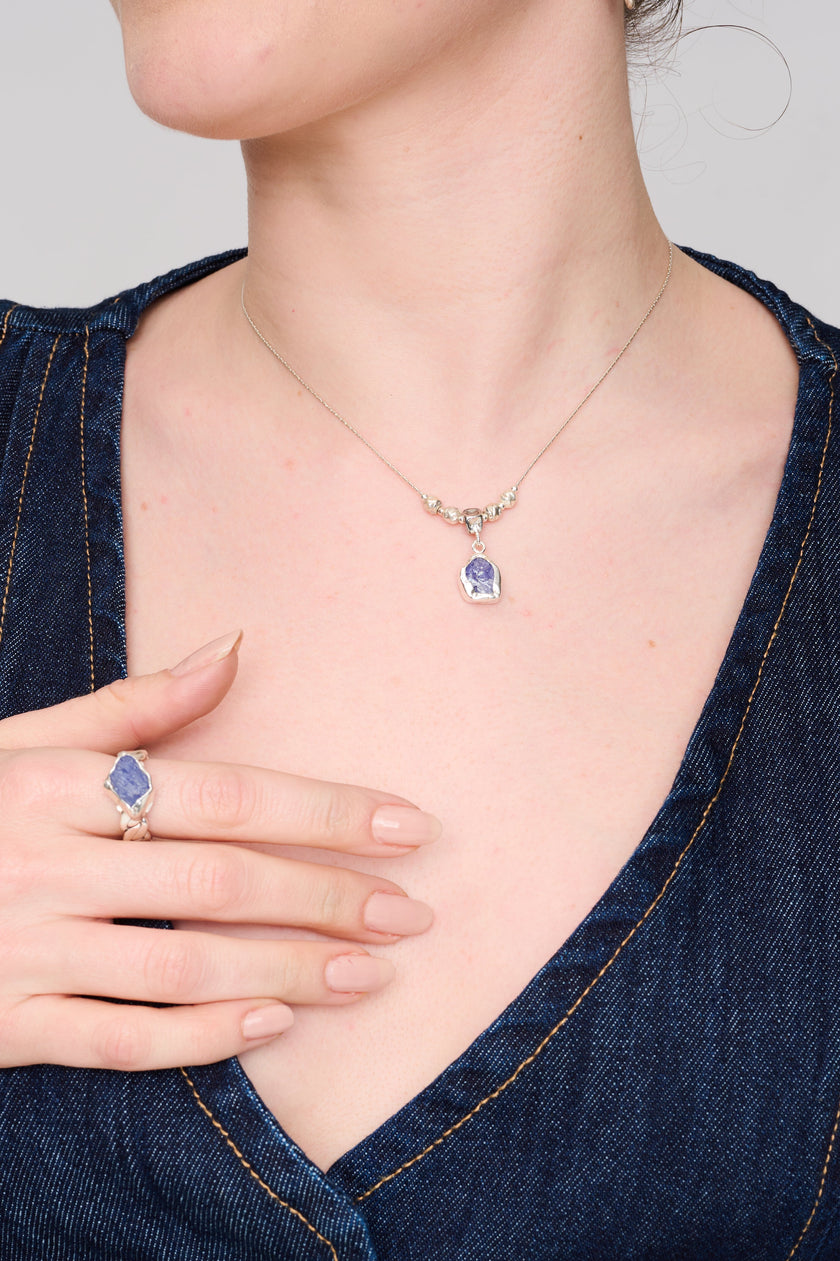 שרשרת בעבודת יד בגימור כסף מבריק, עם אלמנט מרכזי של חמישה חרוזים עגולים במראה מתכתי חלק. מתחתיהם תלוי תליון עגול קטן המשובץ באבן חן כחולה טבעית בגוון תכלת כהה עם טקסטורה קריסטלית. האבן נראית כאילו נחתכה ישירות ממינרל גלם ומוסיפה לתכשיט קסם אורגני. העיצוב מאופק אך מדויק – מתאים למראה יומיומי עם נגיעה של יוקרה רגועה.
הטבעת להמחשה בלבד