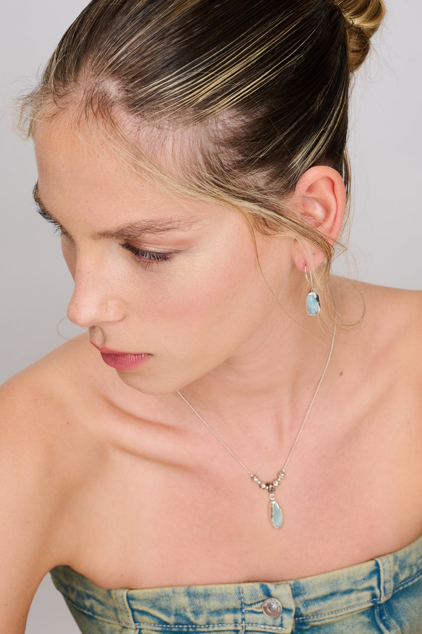 תמונה של שרשרת בעיצוב אומנותי עם תליון מאבן תכלת לא מלוטשת במסגרת כסף מעוגלת, וחרוזים בעלי מרקם טבעי לאורך מרכז השרשרת. שילוב הרמוני של חומרים טבעיים ועבודת צורפות עכשווית, לתחושת אלגנטיות רגועה ונוכחות מתוחכמת.