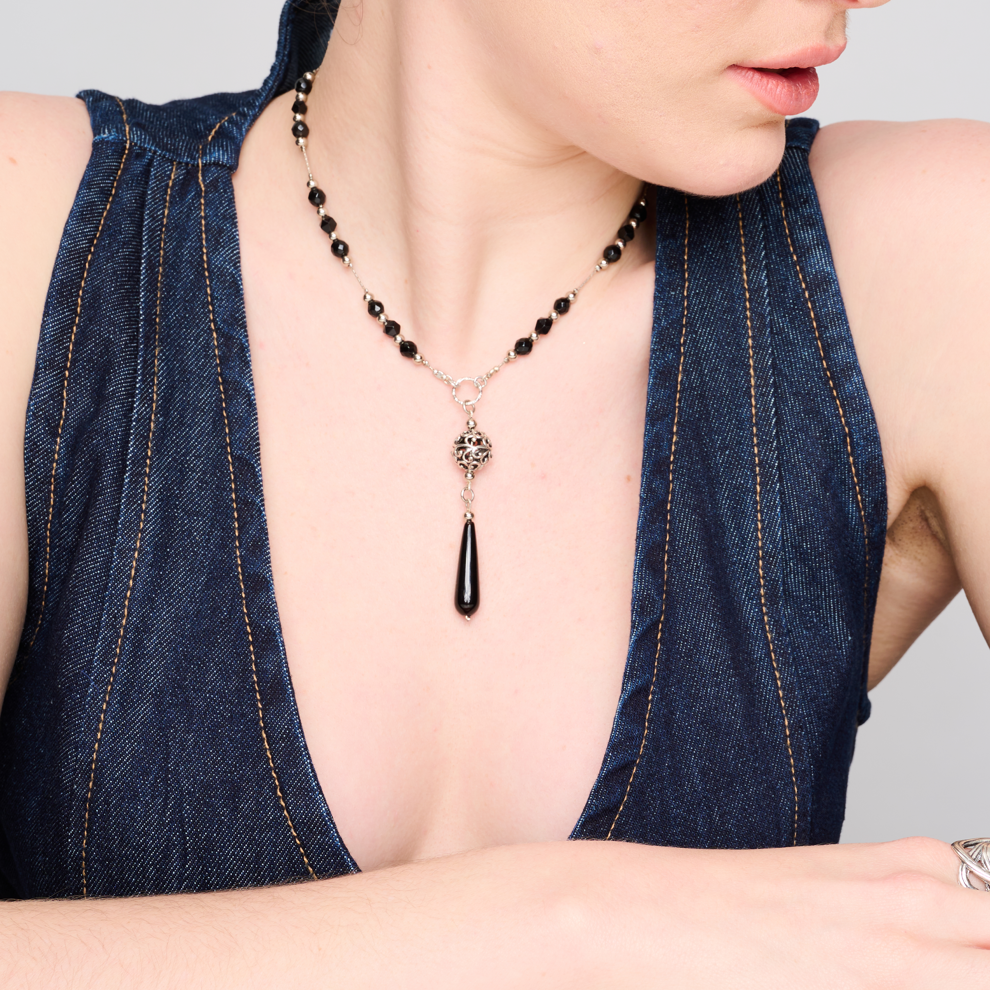 תמונה של שרשרת כסף עם חרוזים עגולים בגוון אדום עמוק, עשויים אוניקס סינתטי מבריק. האלמנטים מחוברים בטבעות כסף מעוצבות, ובמרכז תליון טיפתי באותו גוון. השרשרת מונחת על צוואר חשוף של דוגמנית לבושה בג'ינס, באווירה צעירה ובולטת.