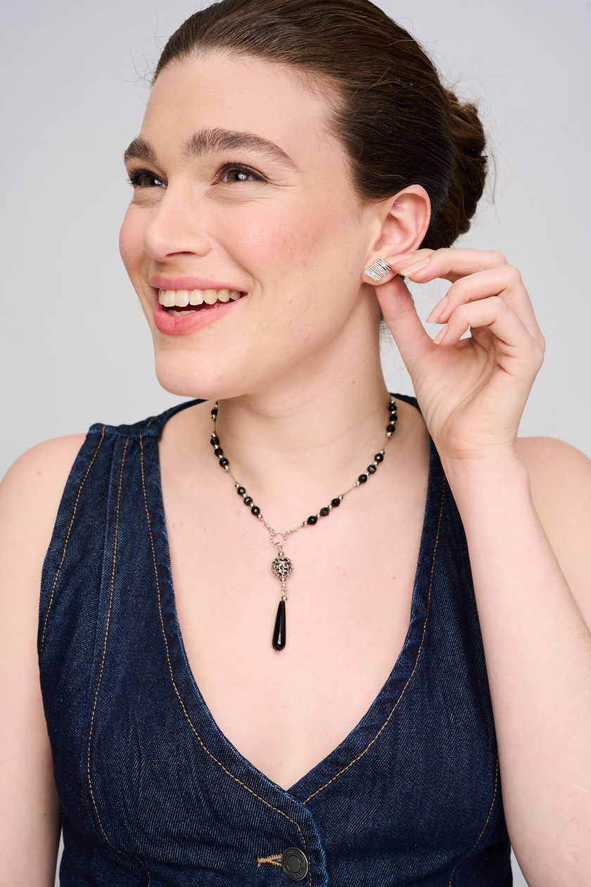 שרשרת בסגנון מודרני-קלאסי, עשויה אוניקס סינתטי אדום, בשיבוץ חרוזים עגולים וטבעת כסף עדינה ביניהם. תליון טיפה ארוך משתלב במרכז. השרשרת מונחת על צוואר של דוגמנית, בצילום המשדר ניגודיות בין ג’ינס יום־יומי לאדום יוקרתי.
העגילים להמחשה בלבד