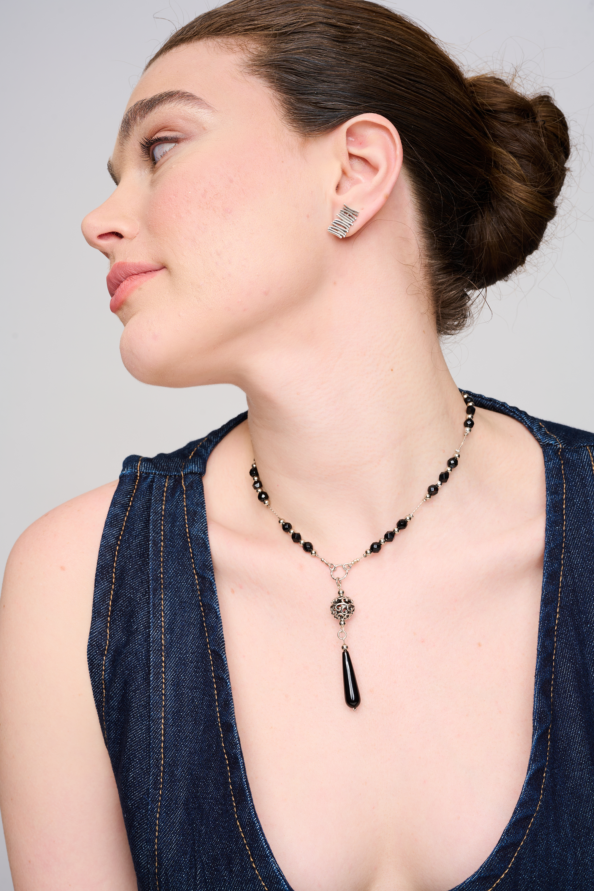 שרשרת בעיצוב גאומטרי־נשי, המורכבת מחרוזים אדומים עשויים אוניקס סינתטי וטבעות מתכת כסופות בגימור מעודן. תליון בצורת טיפה משתלשל למרכז החזה. התכשיט משתלב באופן הרמוני עם עור בהיר ובגד קז'ואלי, ויוצר מראה עוצמתי ומעודן.