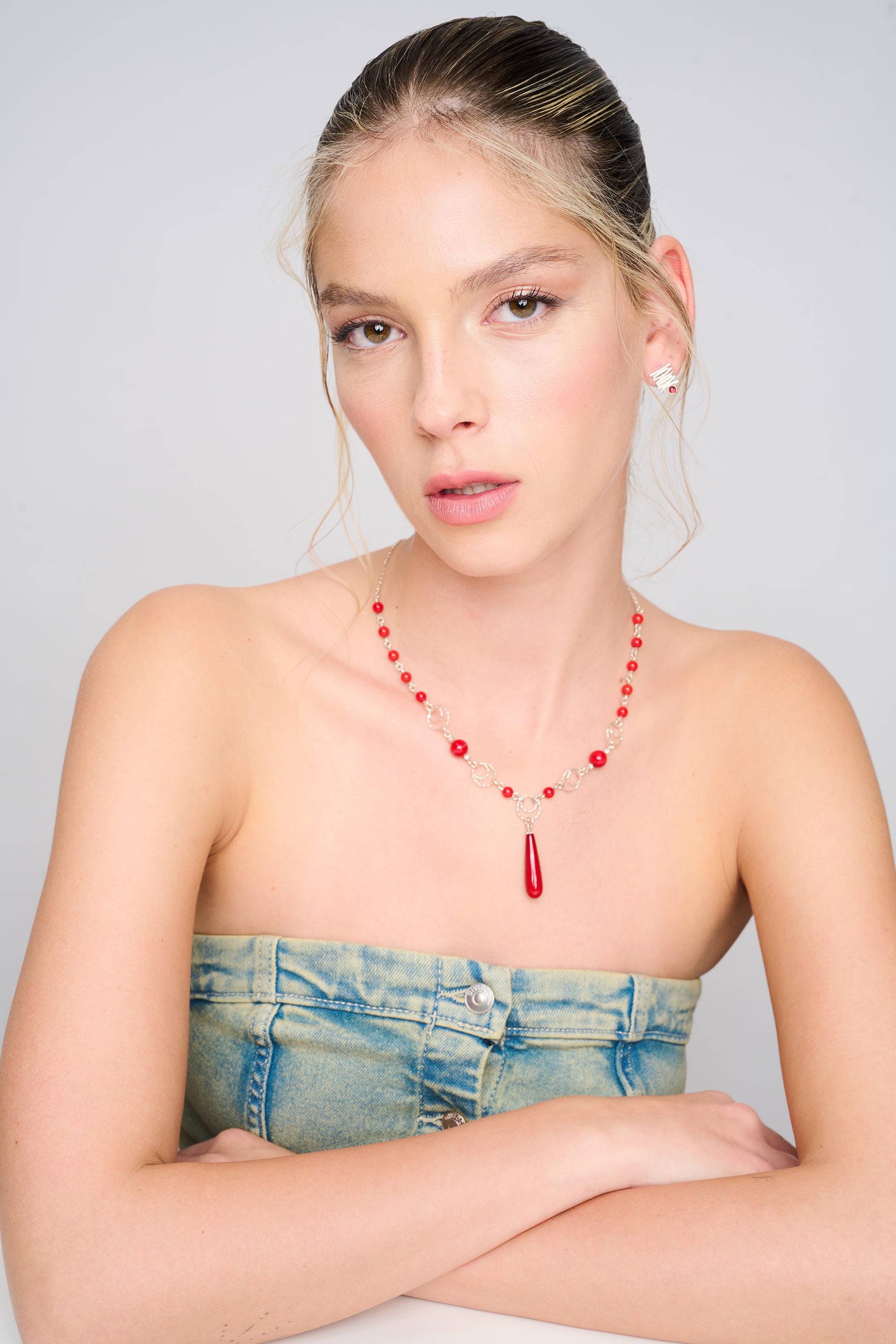 שרשרת כסף עדינה אך בולטת, מעוטרת בחרוזים אדומים מאלמוג סינתטי, כולל תליון טיפתי המשתלשל ממרכז השרשרת. העיצוב משלב בין תנועה לבין צבעוניות חזקה, ומתאים למראה יום-יומי עם נגיעה של יוקרה. הרקע הוא גוף חשוף עם חלק עליון מג'ינס.