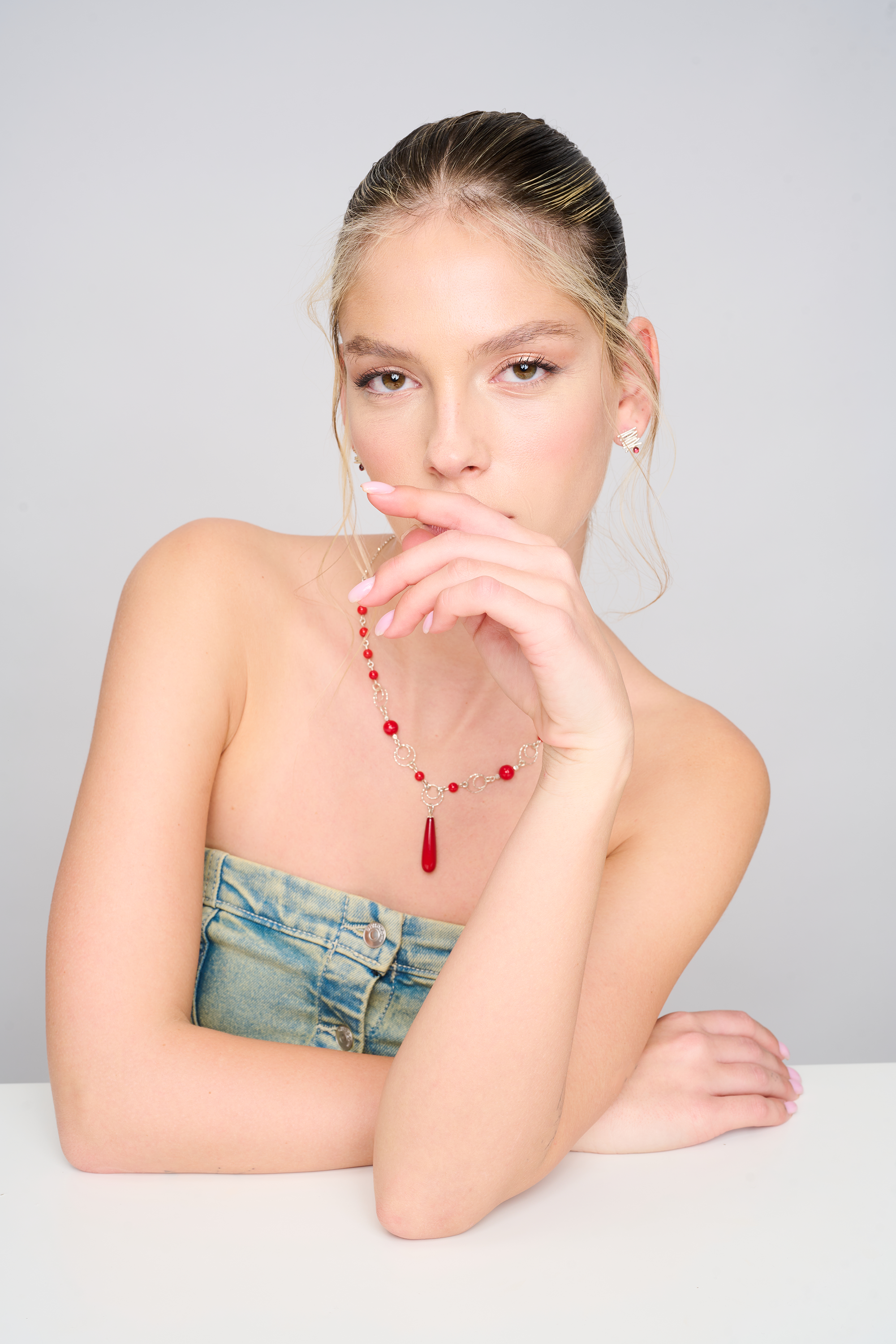 תמונה של תכשיט בעל נוכחות – שרשרת כסף עם חרוזי אלמוג סינתטי בגוון אדום חי. השרשרת מורכבת מטבעות כסופות מעוגלות וחרוזים עגולים, עם תליון טיפה במרכז. מוצגת על צוואר של דוגמנית בלבוש קז'ואל, המבליט את צבע האבן הסינתטית.