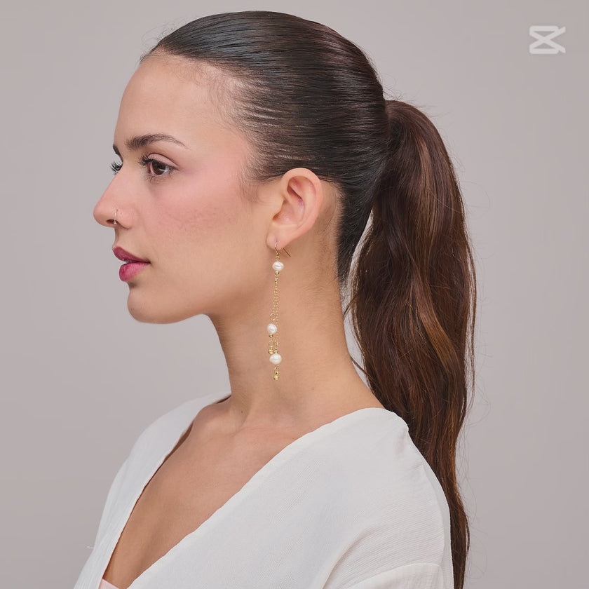 עגיל תלוי בעיצוב עשיר ומעודן המשלב שרשראות זהב דקות עם פנינים טבעיות בגוון לבן שמנת. כל פנינה מופרדת בחרוזי זהב מבריקים ליצירת מראה אלגנטי, קליל ונשי. מתאים ללבישה עם שמלה קלאסית, בגדי ערב או מראה רומנטי ביום-יום. עיצוב ייחודי שמעניק תחושת זרימה ותנועה מרשימה.

