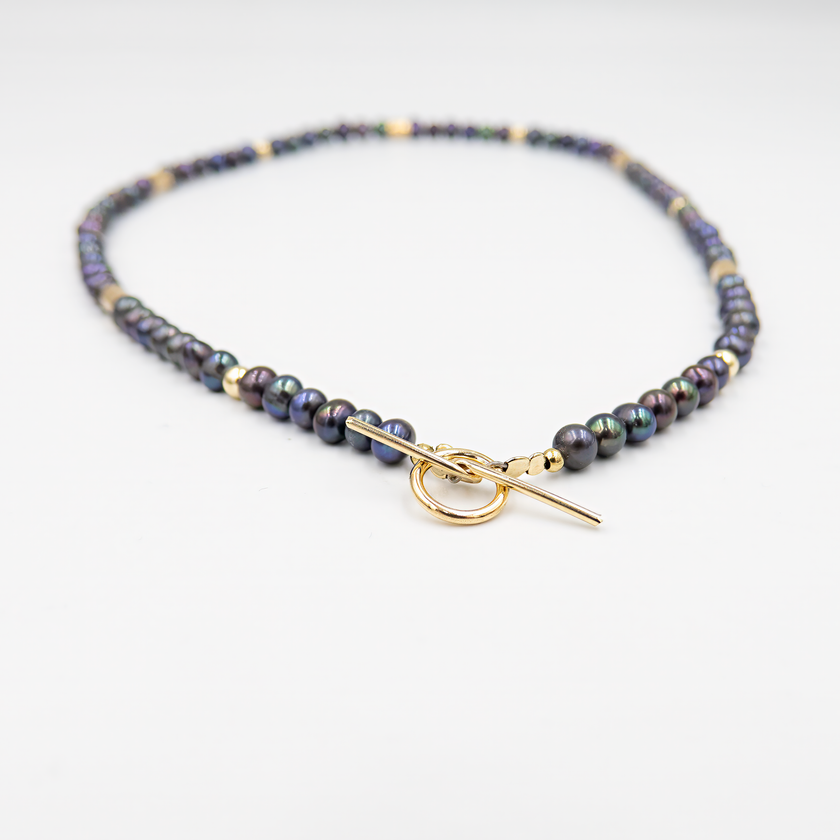 שרשרת צמודה עם פנינים שחורות ואלמנטים מוזהבים – קולר עם אמירה מסוגננת, שמשלב בין עומק אלגנטי לנגיעה חמימה של זהב. הפנינים השחורות יוצרות נוכחות דרמטית אך הרמונית, ואילו חרוזי הגולדפילד מוסיפים קונטרסט זוהר ושיק עכשווי. העיצוב הצמוד לצוואר מדגיש את קווי המתאר ומעניק מראה נשי, חזק ומתוחכם. תכשיט למראה חגיגי או כטאץ’ מדויק ביומיום.