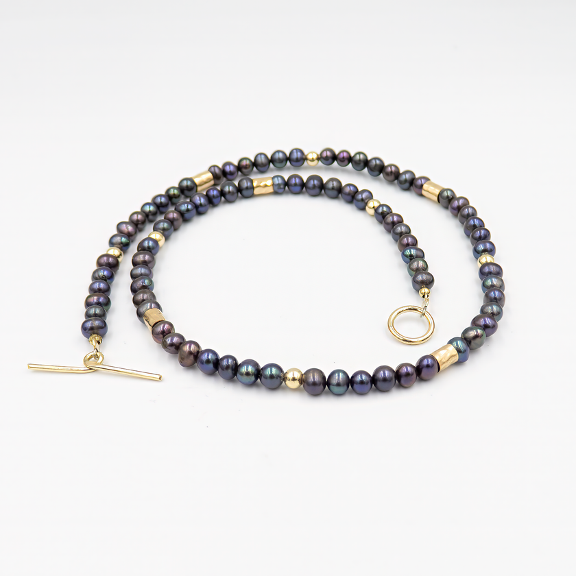 עיצוב יוקרתי עם שילוב של פנינים כהות וזהב – קולר עם אמירה מסוגננת, שמשלב בין עומק אלגנטי לנגיעה חמימה של זהב. הפנינים השחורות יוצרות נוכחות דרמטית אך הרמונית, ואילו חרוזי הגולדפילד מוסיפים קונטרסט זוהר ושיק עכשווי. העיצוב הצמוד לצוואר מדגיש את קווי המתאר ומעניק מראה נשי, חזק ומתוחכם. תכשיט פריט ורסטילי שמשדר יוקרה ורוך.